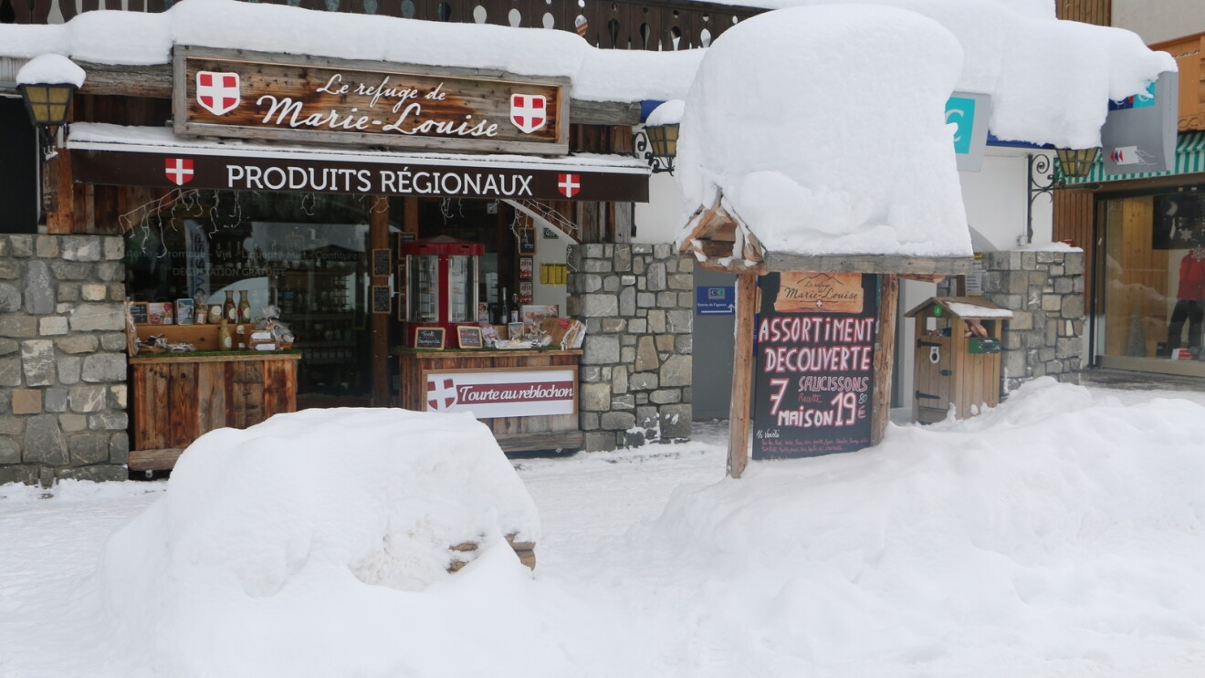 Snowy scene showing "La refuge de Marie-Louise" signage on a quaint shop 
