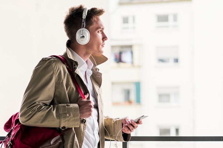 A stylishly dressed man listens to audio from his smartphone via headphones