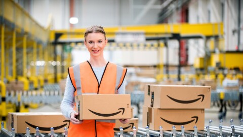 Uśmiechnięta pracowniczka Amazon trzymająca zapakowane zamówienie, w tle centrum logistyki.