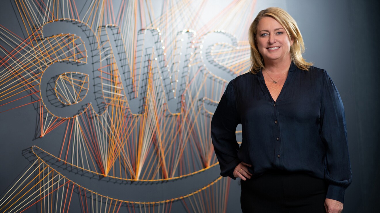 An image of a woman smiling for a photo in front of a wall that says "AWS" in string.