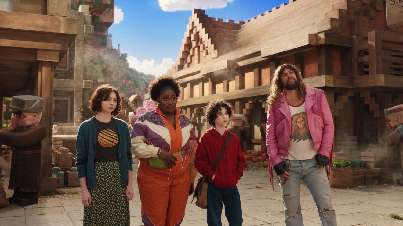 A Minecraft Movie characters in colourful outfits standing on a street with wooden buildings