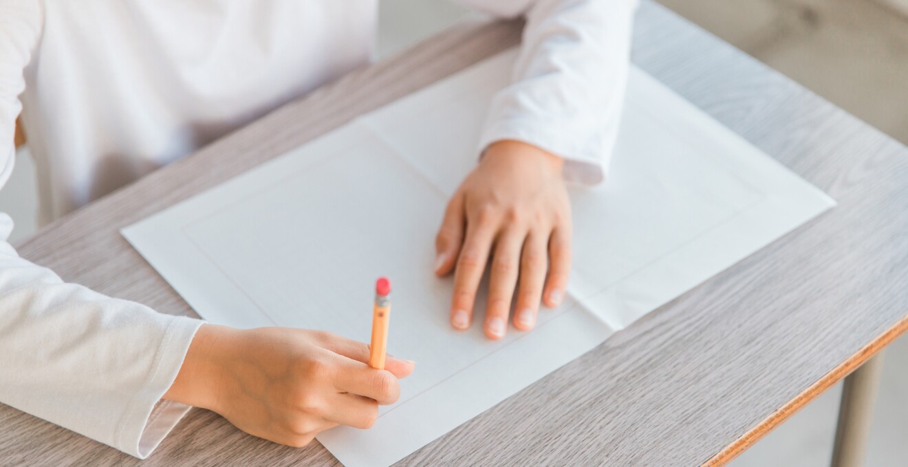 机の上で原稿用紙に鉛筆で書き込もうとしている子どもの手