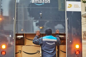 An image of a man closing the back of an Amazon delivery truck that is loaded with Amazon boxes inside of it.