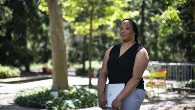 一名穿着牛仔裤和背心的女子双臂抱着笔记本电脑,看着镜头。