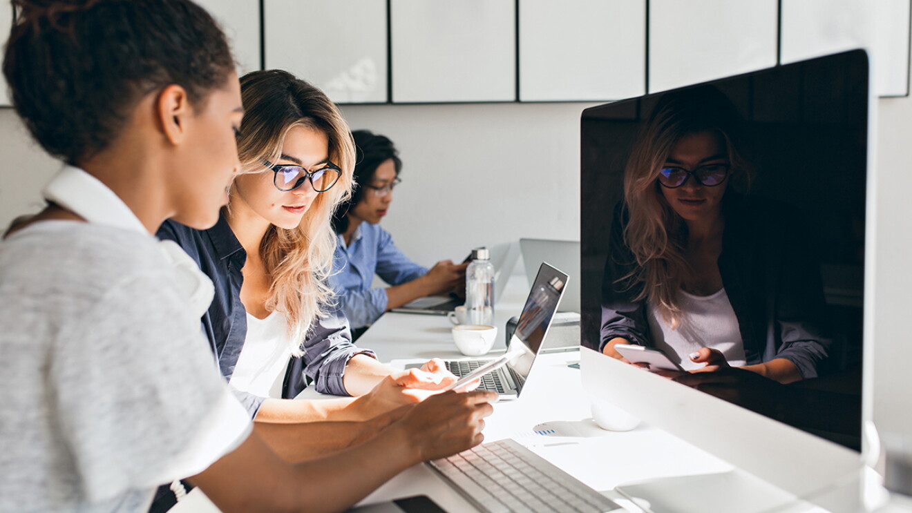 Three young women work at computers in a clean, white setting. Image taken pre-COVID-19 pandemic.
