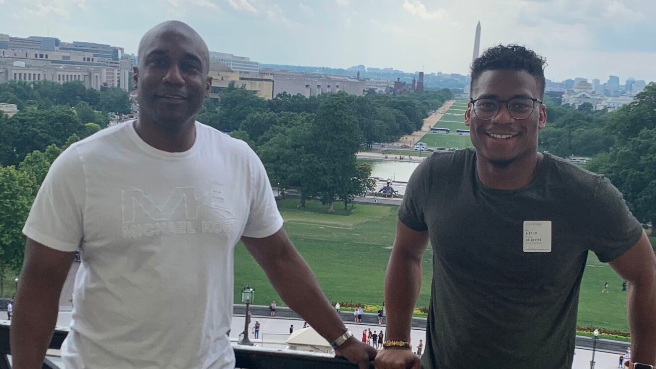 Jaren Kirkland stands next to his dad on a balcony with the Washington Monument behind them in the distance.