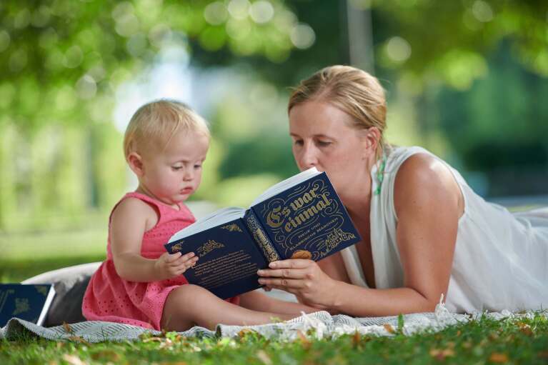 Eine Mutter liest auf einer Picknickdecke ihrem kleinen Kind etwas vor
