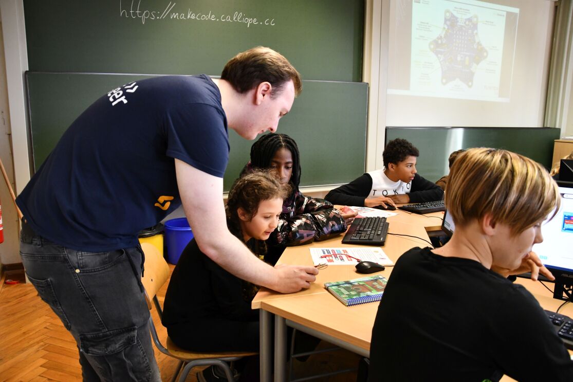 Ein Amazon Mitarbeiter redet mit drei Kindern und einer Erwachsenen an einem runden Tisch.