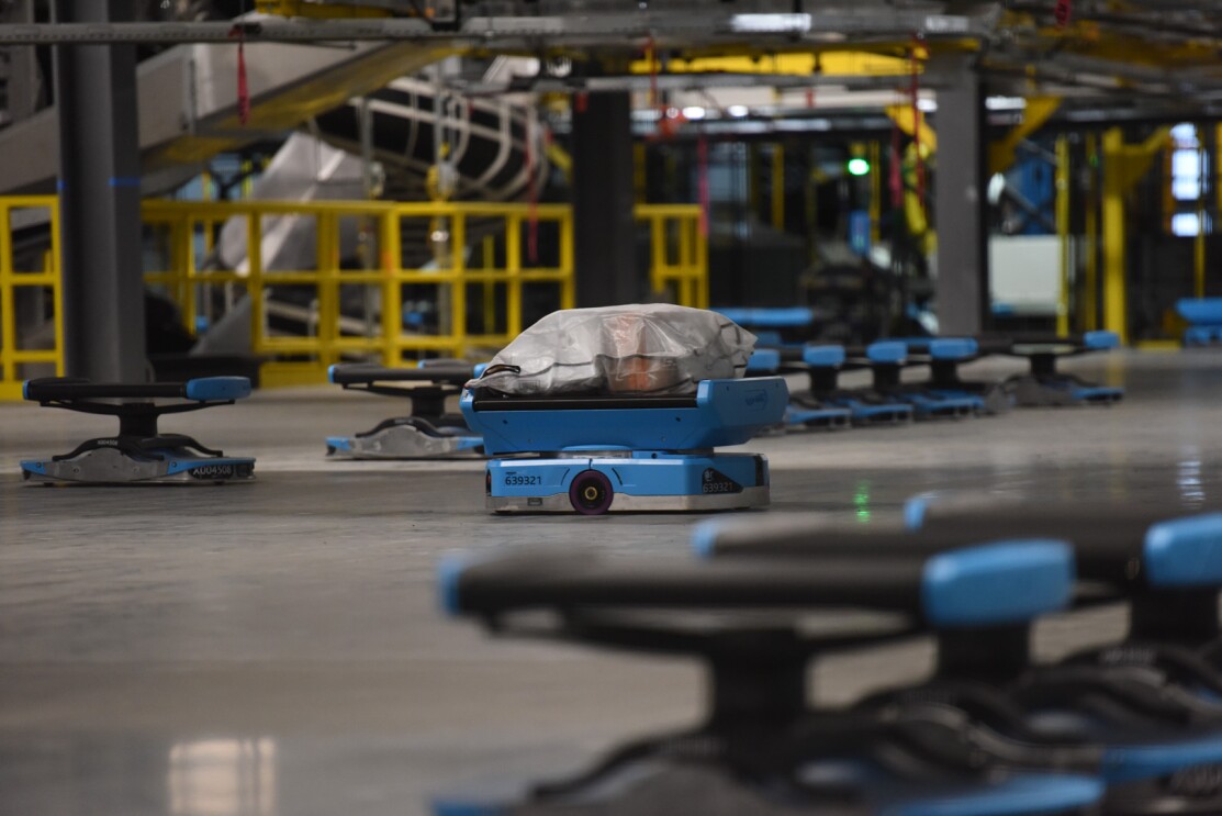An image of small, blue robots with packages on them rolling through an Amazon sortation center.
