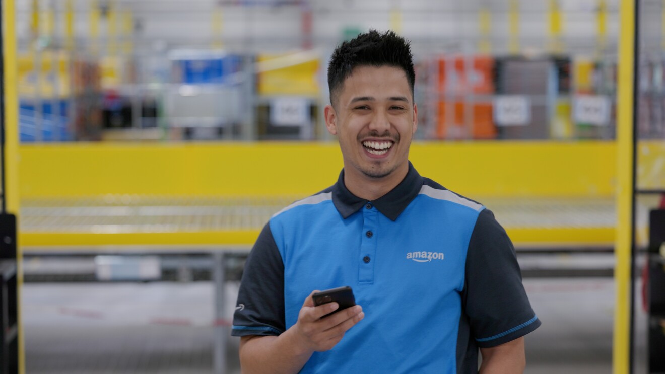 Ein Lieferfahrer mit blauem Amazon Shirt liest Nachrichten auf einem Handy.