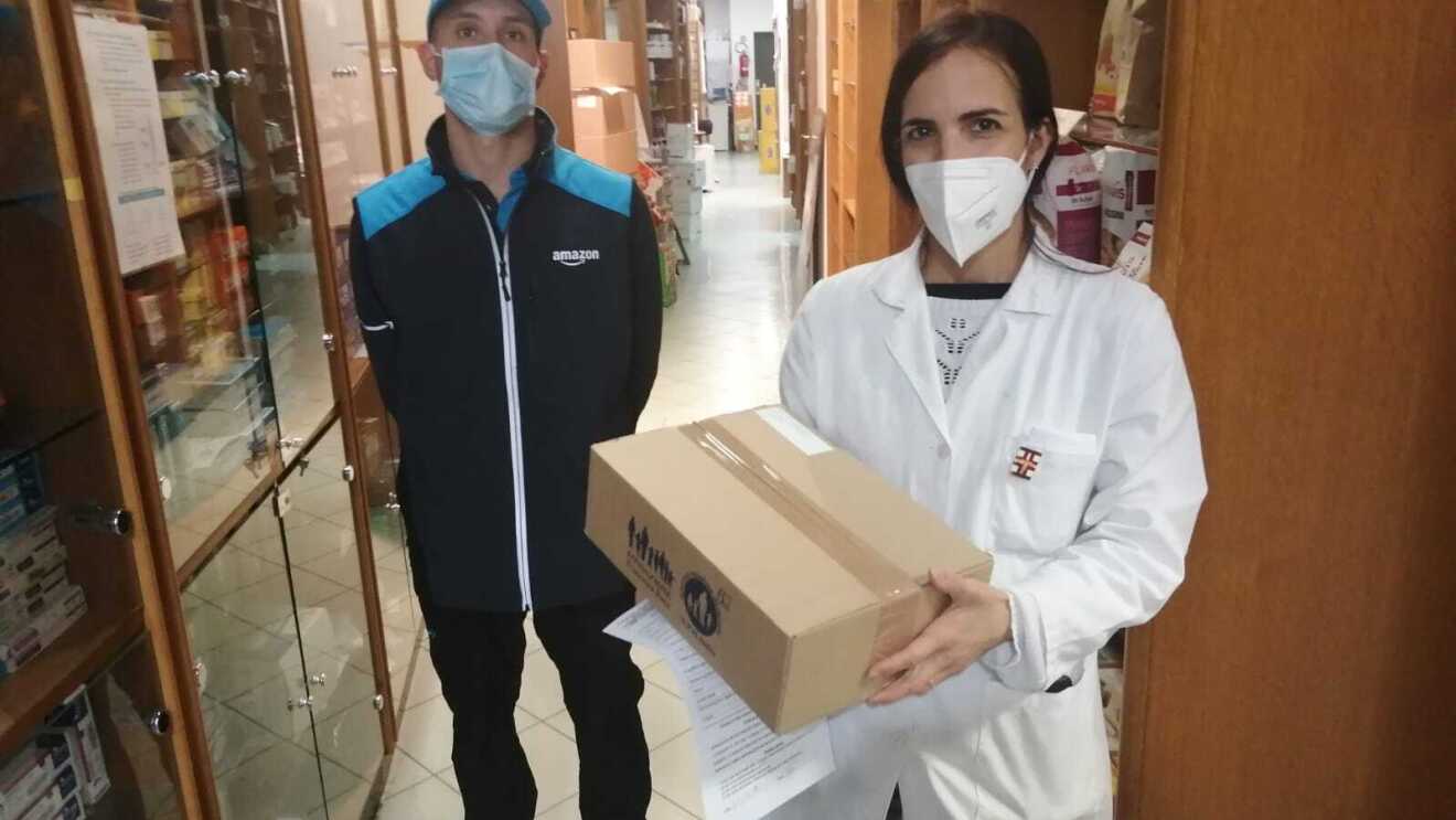 Un autista Amazon consegna un pacco di medicinali ad una farmacista, che indossa un camice bianco.