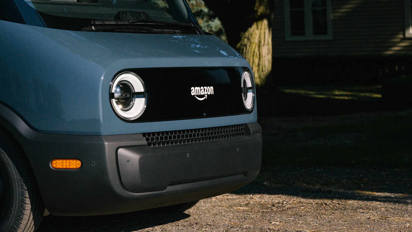 Primer plano de la parte frontal de la furgoneta Rivian. Aparecen los dos faros en blanco y en el centro del logo de Amazon también en blanco. La parte inferior de ventilación es de color negro. 
