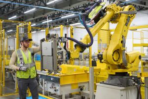 An Amazon employee in safety vest interacting with robotic equipment at a robotics facility