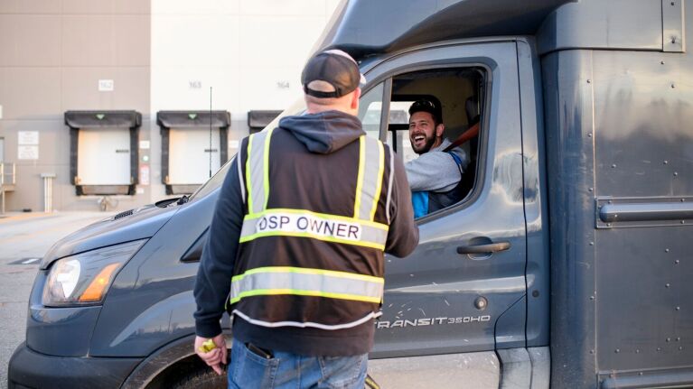 DSP owner greets smiling delivery driver in vehicle at loading dock