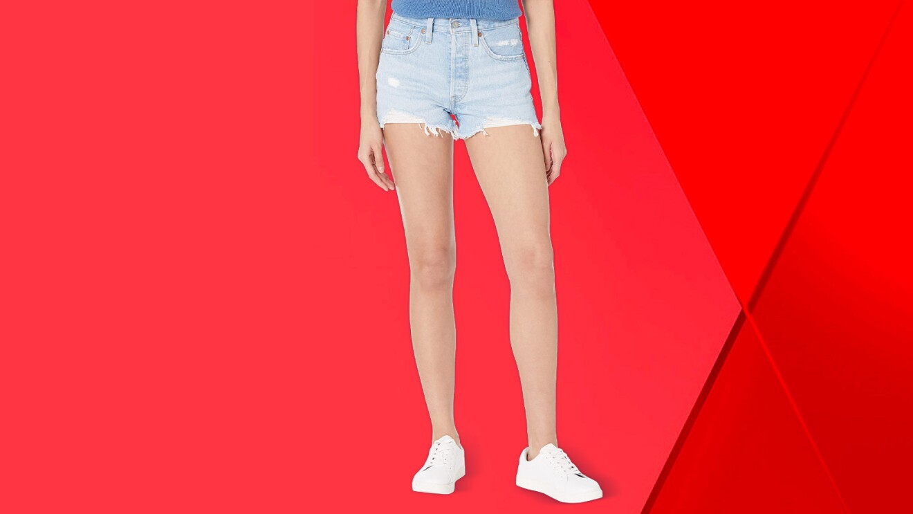 Woman's legs in denim shorts and white sneakers against red background