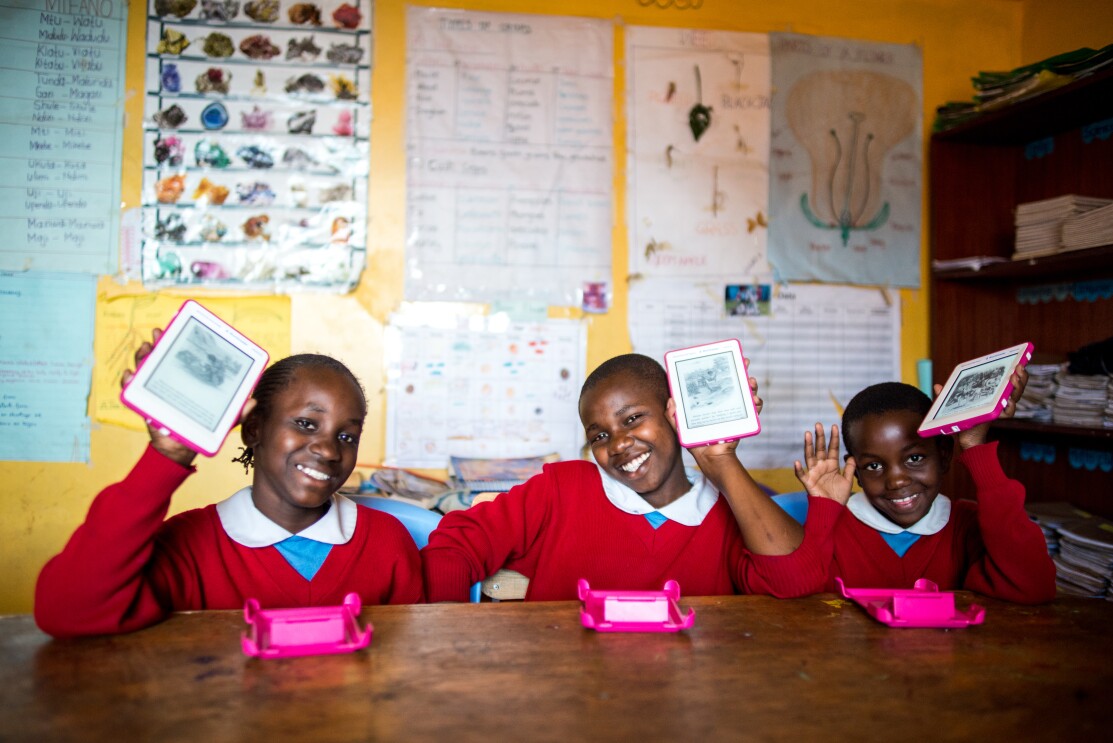 Three smiling girls in read school uniforms with white collars hold up their Kindle Worldreaders.