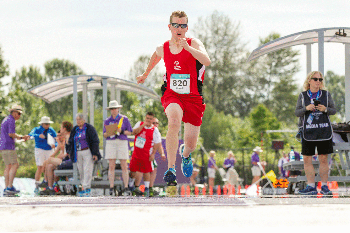 An image of a person running in a race. There are people standing on the background.