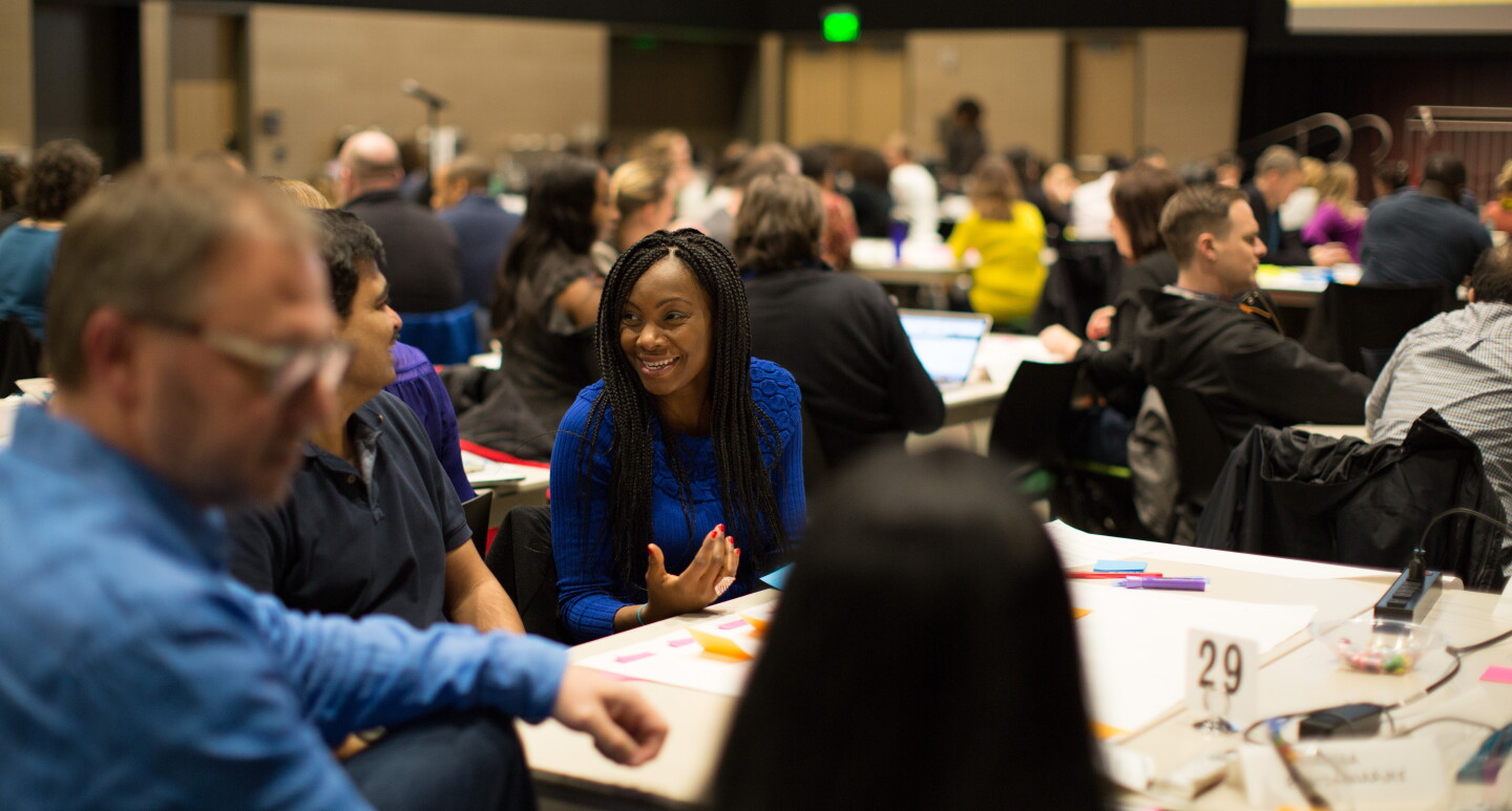 Men and women gather together at tables in a conference setting