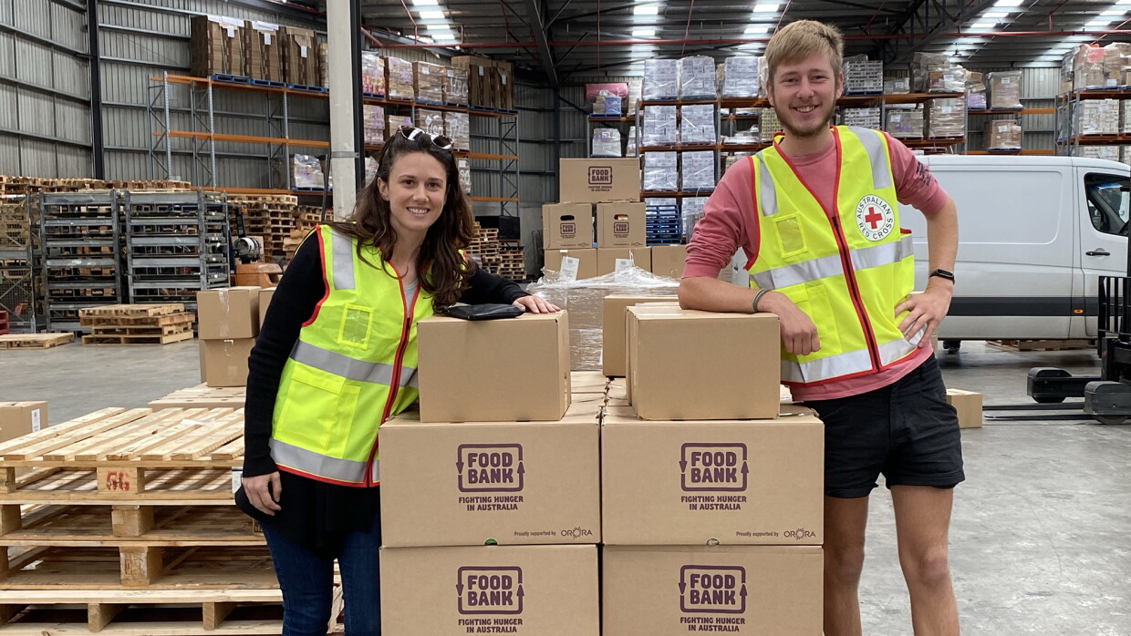 A woman and a man, both wearing a yellow safety vest, pose next to a pallet of boxes that have "food bank" printed on the front. 