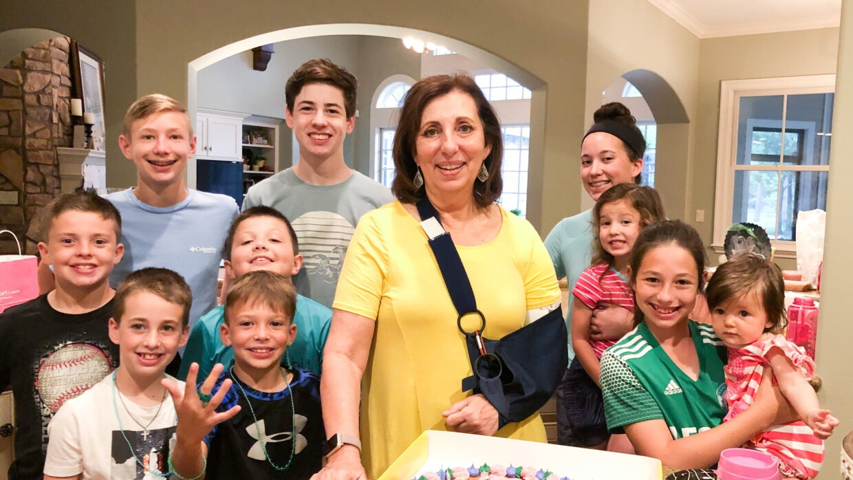 Rebecca en un cabestrillo que sostiene su brazo izquierdo está rodeada por sus diez nietos con un pastel de cumpleaños frente a ellos.