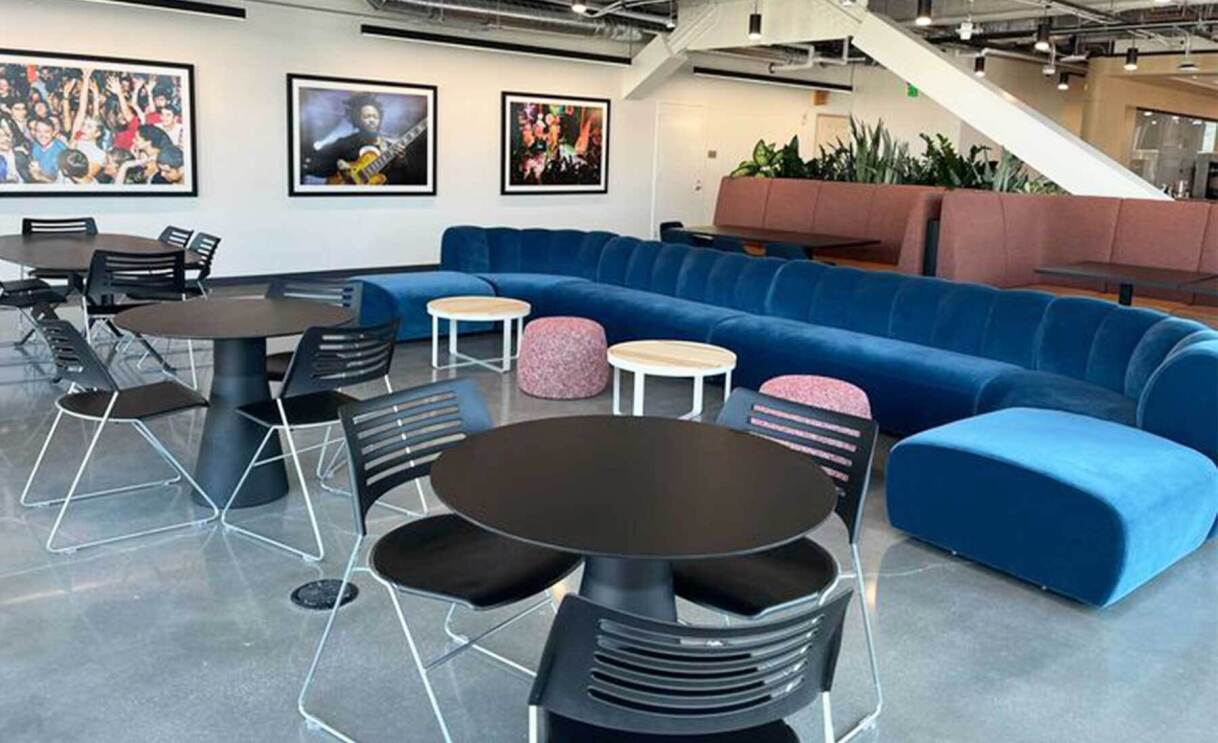 An image of a large room with a large velvet, blue couch and artwork showing concerts on the wall.