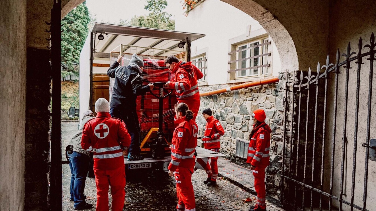 6 Mitarbeiter vom Roten Kreuz stehen hinter einem Rettungswagen.