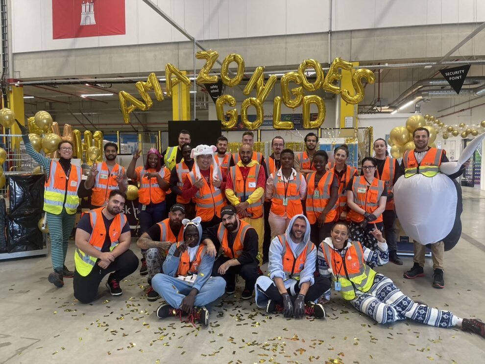 Man sieht eine Gruppe von Amazon Mitarbeiter:innen im Schlafanzug, die vor goldenen Luftballons posieren.