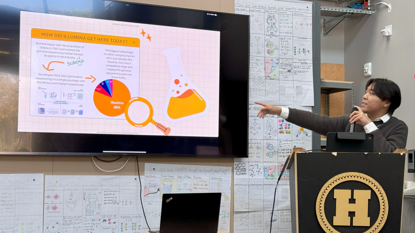 Young presenter at podium pointing to Illumina company timeline on large screen