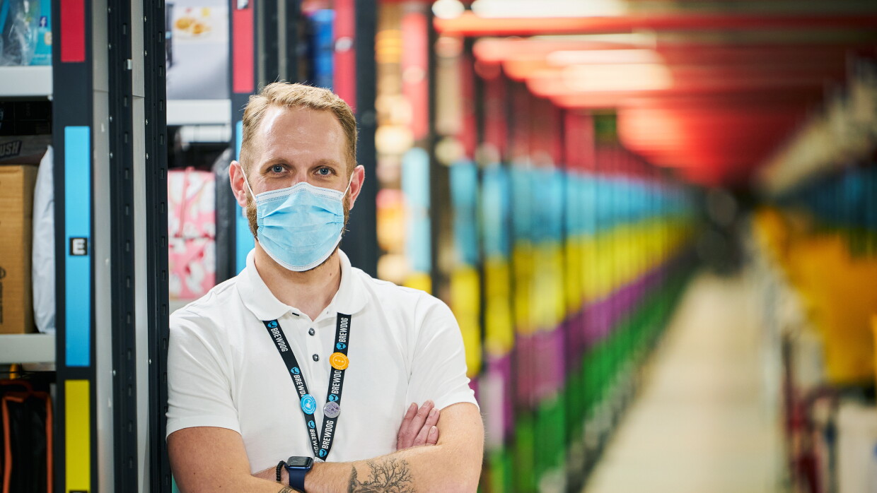 Craig Urquhart, Operations Manager at Amazon's fulfilment centre in Dunfermline, pictured cross-armed with colourful aisles blurred in the background