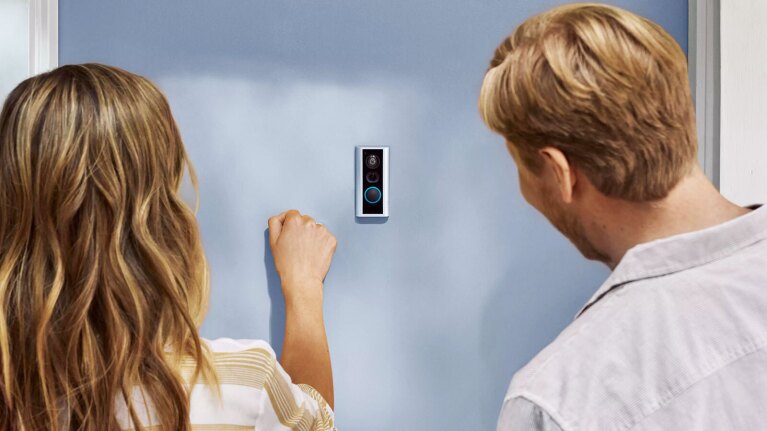 an image of two people knocking on a door. There is a Ring Peephole Camera in the middle of the door.