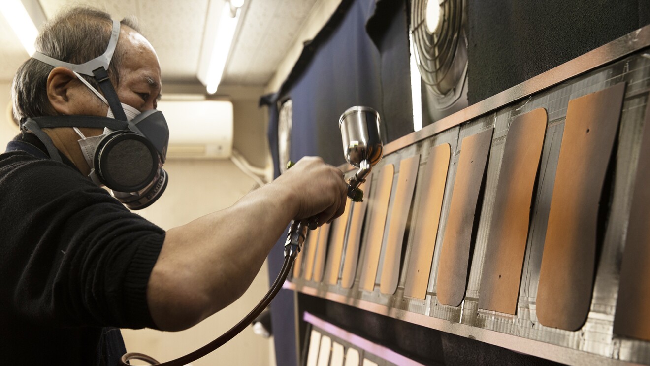 特殊なマスクをつけ、並べられた裁断済みの革をスプレーで染めていく職人の写真