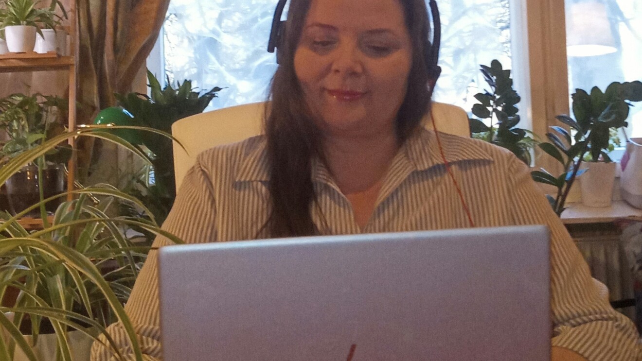 Eine Frau mit Kopfhörern sitzt an einem Tisch und schaut in ihren Laptop.
