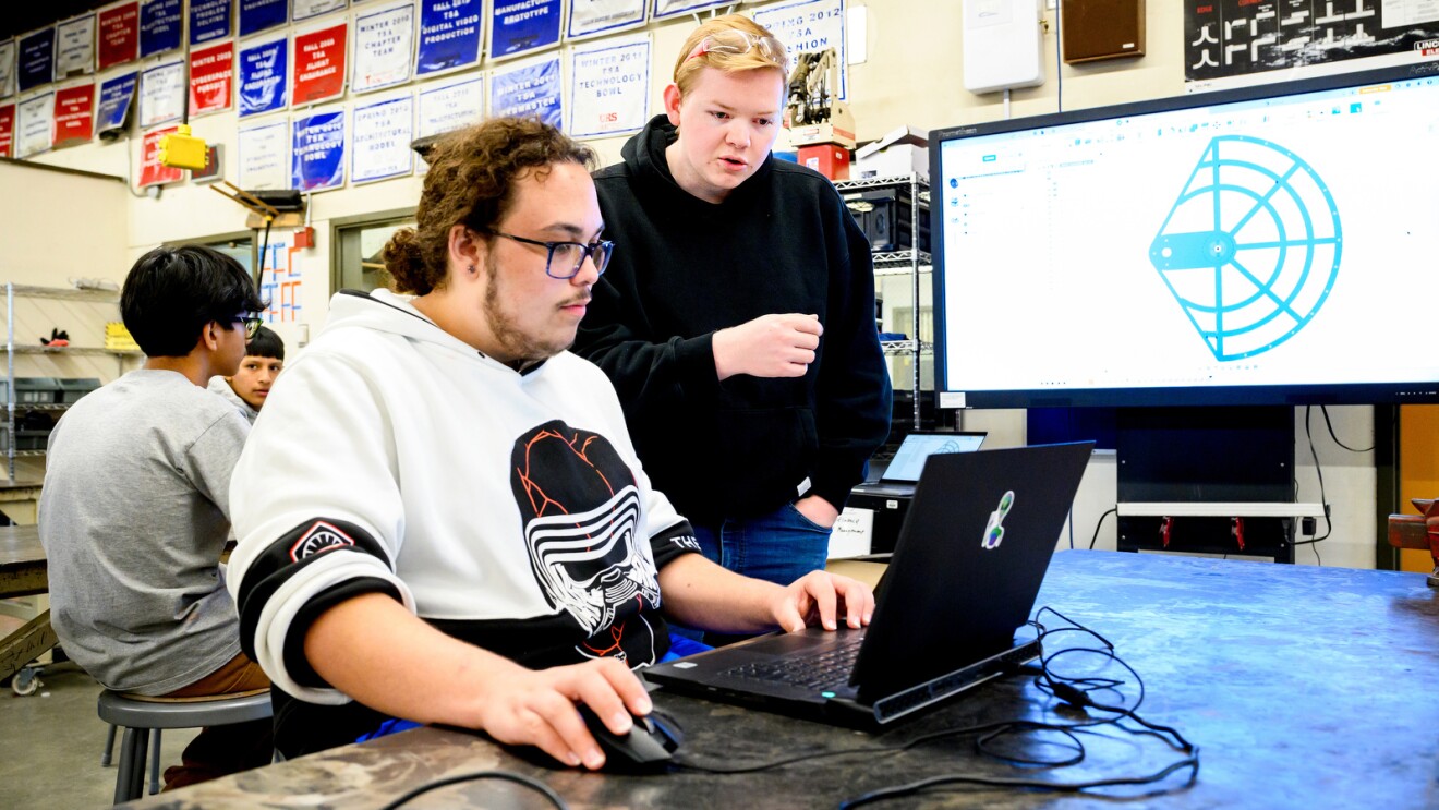 A photo of two students working on a computer in a high school robotics lab.