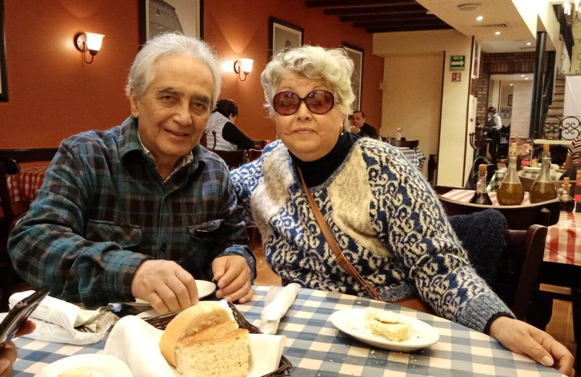 An image of a couple smiling for a photo while eating dinner at a restaurant. 