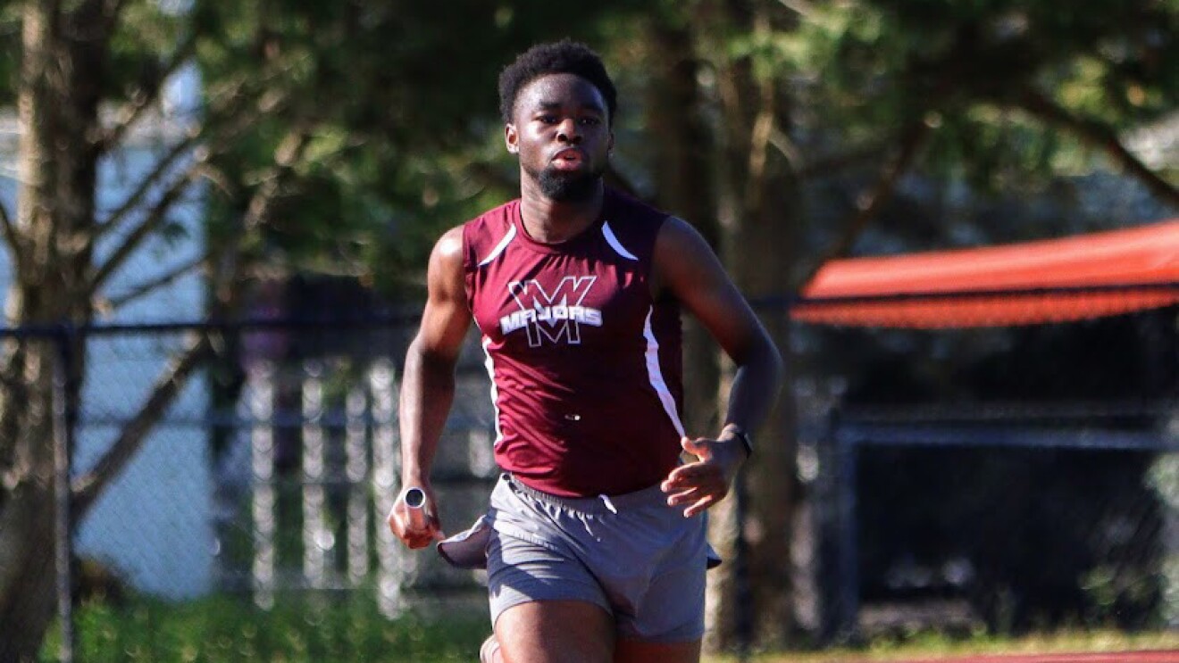 An image of a young man running on a school track wearing a track team uniform.