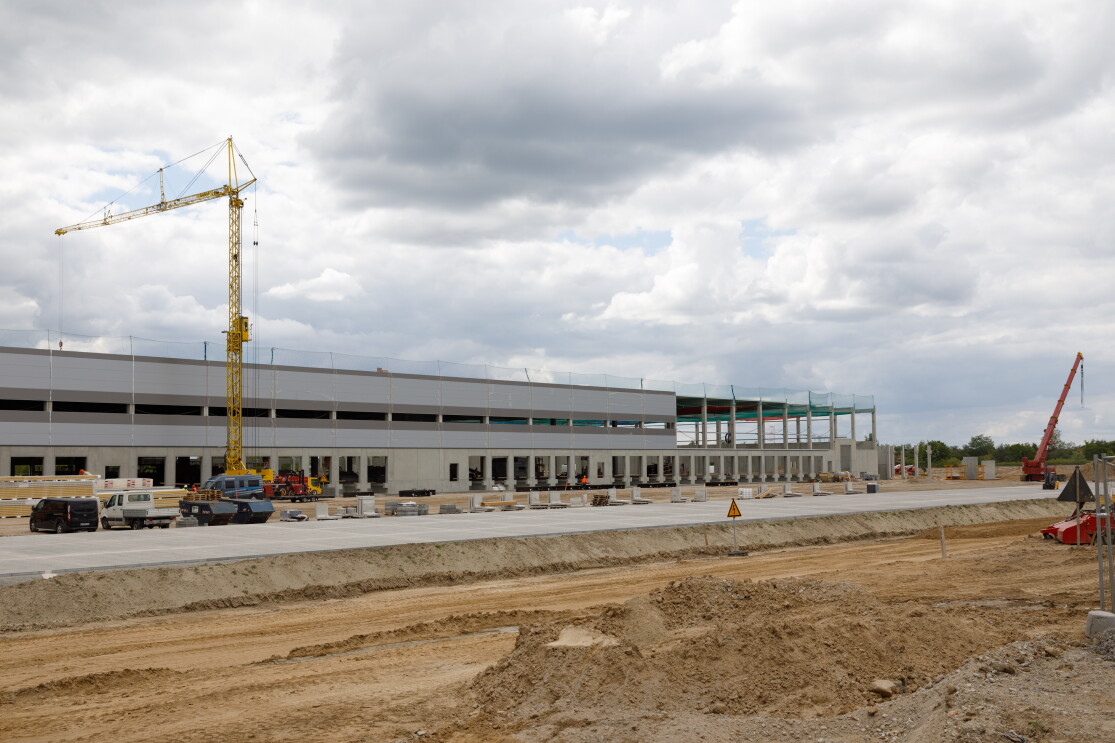 Bagger, Kräne und Baustellenfahrzeuge sind vor einem lang gestreckten Gebäude