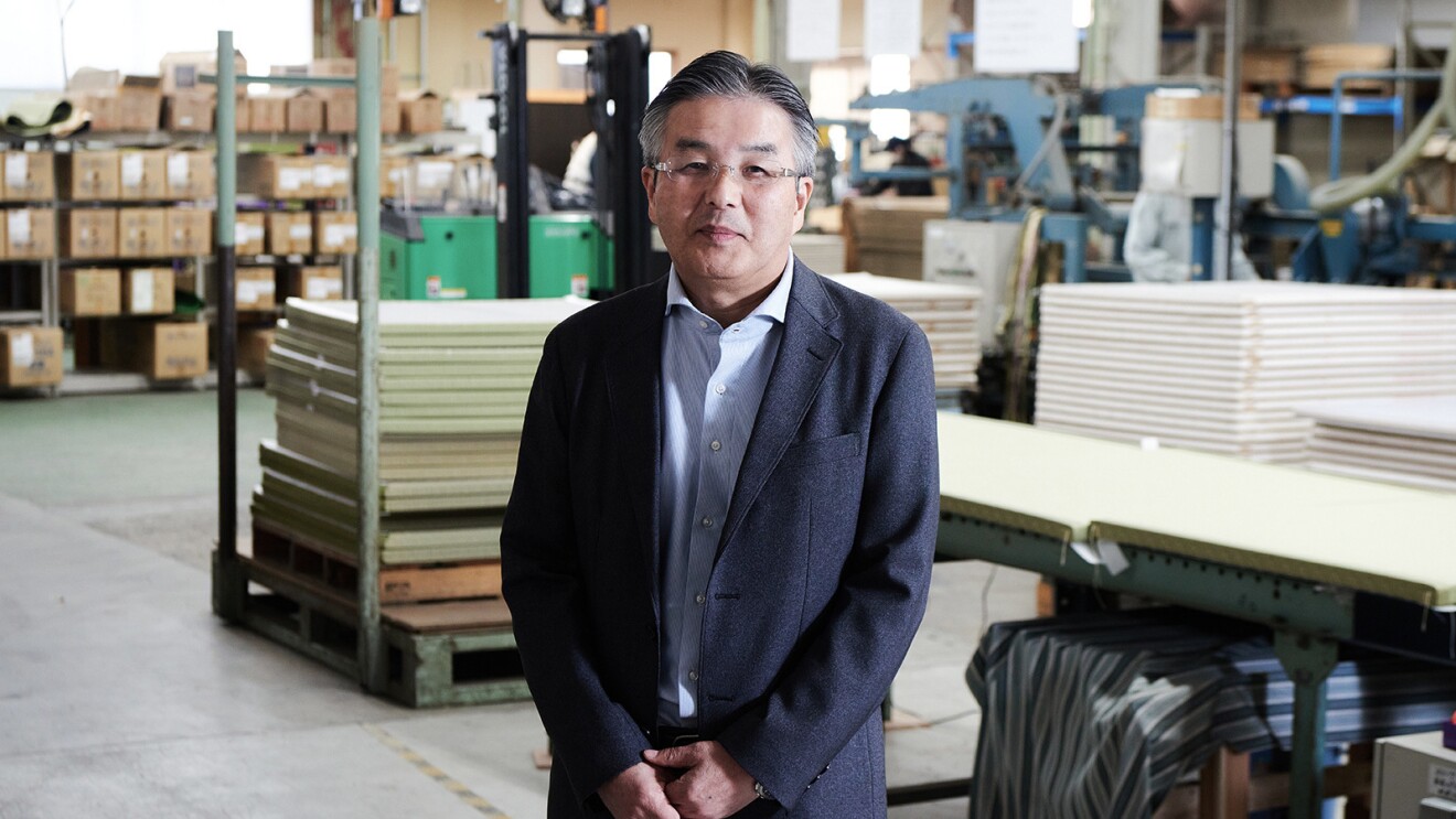 畳が並ぶ工場に立つスース姿の男性