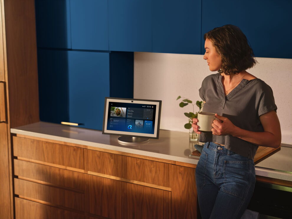 Woman in kitchen holding coffee talking to Alexa+