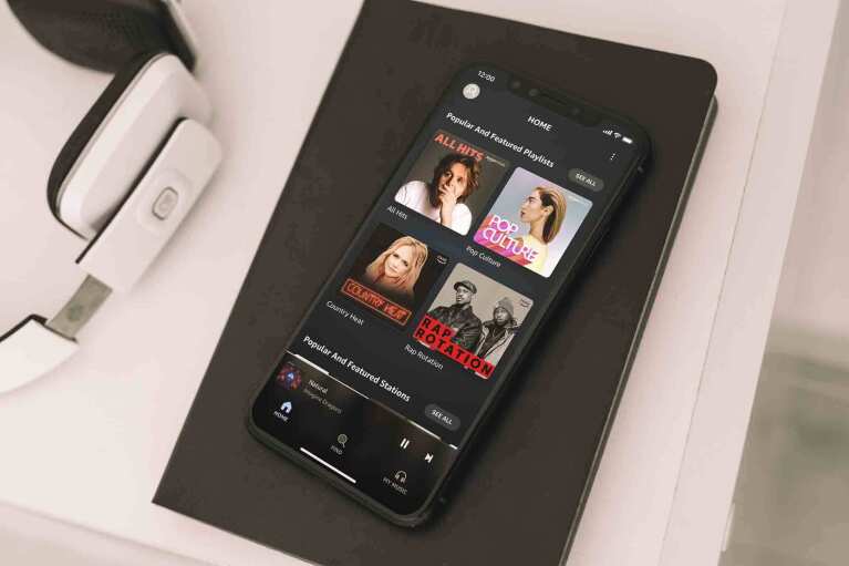 Amazon Music app on an iPhone X displayed on a notebook next to a pair of headphones.