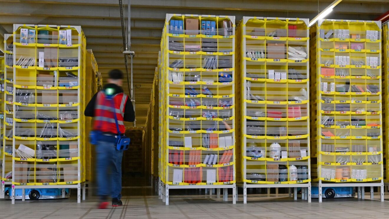 Ein Logistikmitarbeiter im Robotics-Bereich läuft zwischen gelben Türmen mit Amazon-Artikeln.