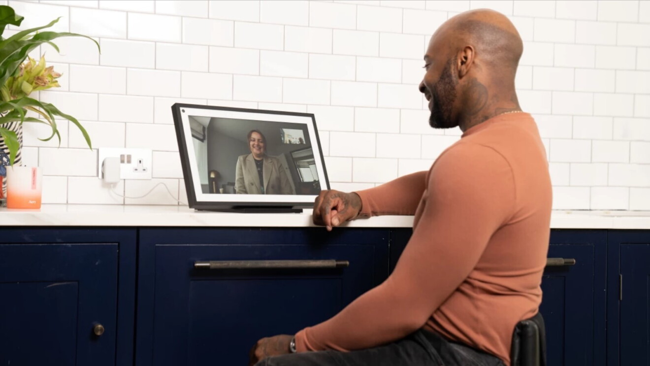 man sits at desk and talks to friend using accessible device