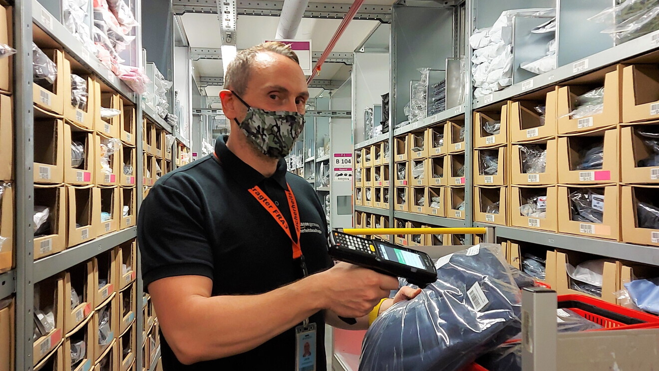 Jens mit schwarzem Poloshirt und Nike-Sporthose sowie in Maske beim Einlagern im Logistikzentrum.