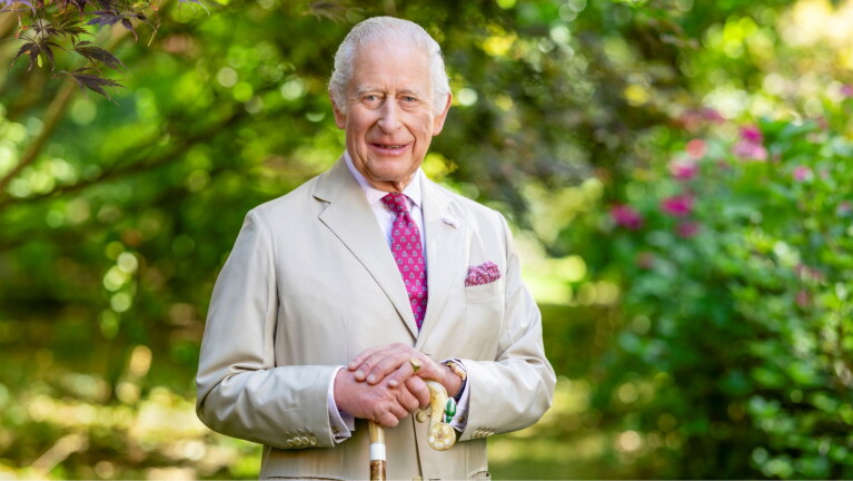 King Charles in light suit smiling in lush garden setting