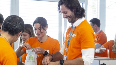 Mehrere Amazon Mitarbeiter:innen in orangenen Volunteer T-Shirts beim Packen von Hygienesets für bedürftige Geflüchtete.