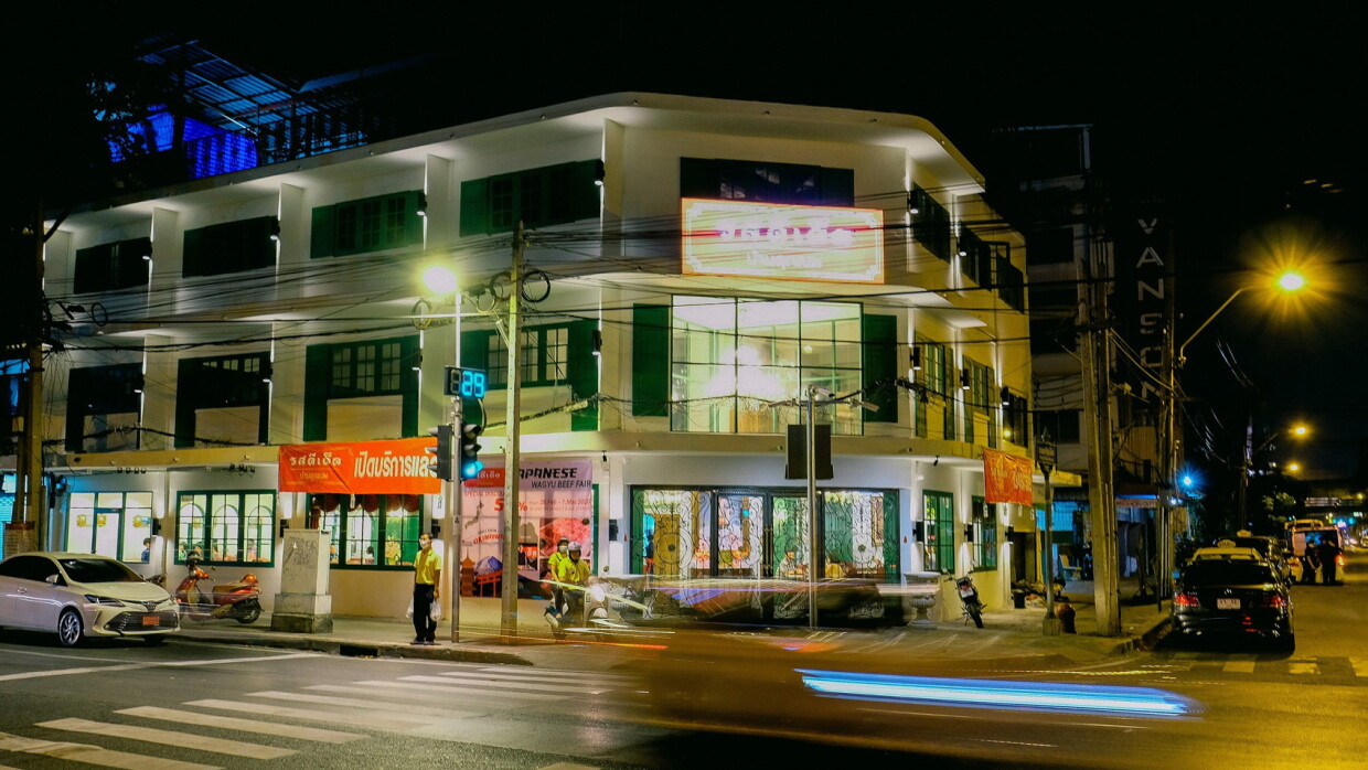 An image of a building with shops on the corner of a street in a city in Thailand.