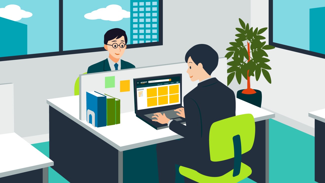 オフィスの中でPCでAmazonサイトを閲覧している男性と、その前にもう1人の男性が座っている