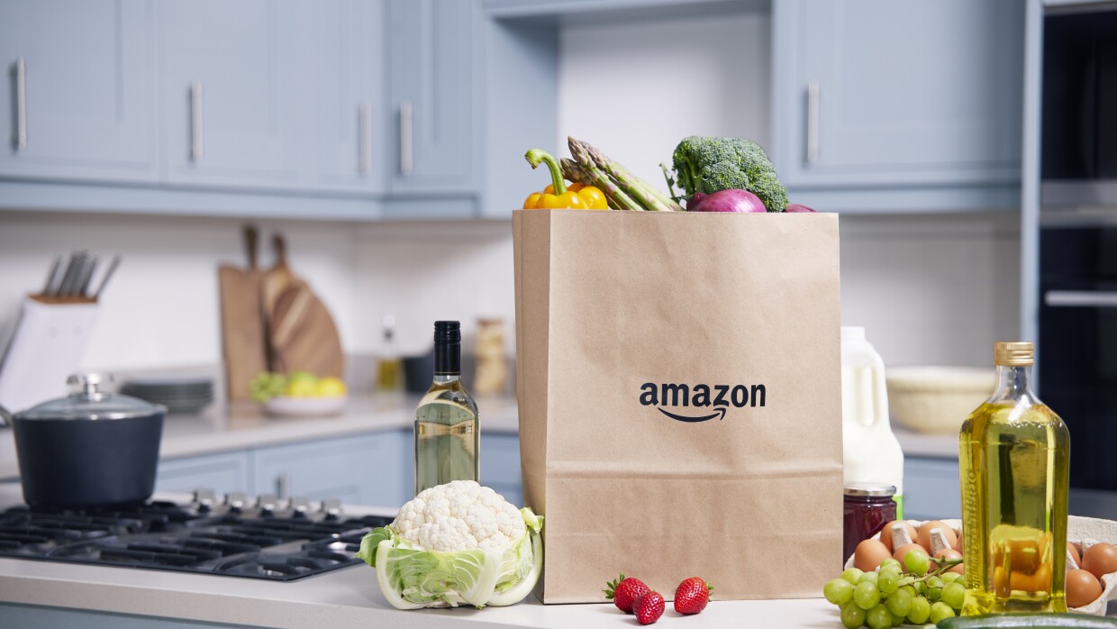 A kitchen counter top with fresh produces like strawberries, cucumber, grapes, eggs and a paper bag with the amazon label on it