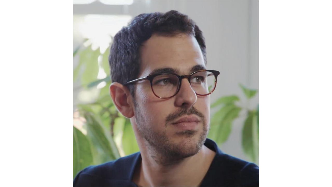 Ezequiel Karpf looks off into the distance and wears eyeglasses. There are houseplants behind him.