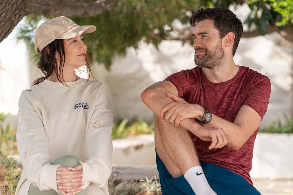 A man and a woman looking at each other sit under a tree