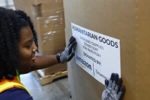 An Amazon employee places a sticker that reads "Humanitarian goods" on a big box filled with relief items.